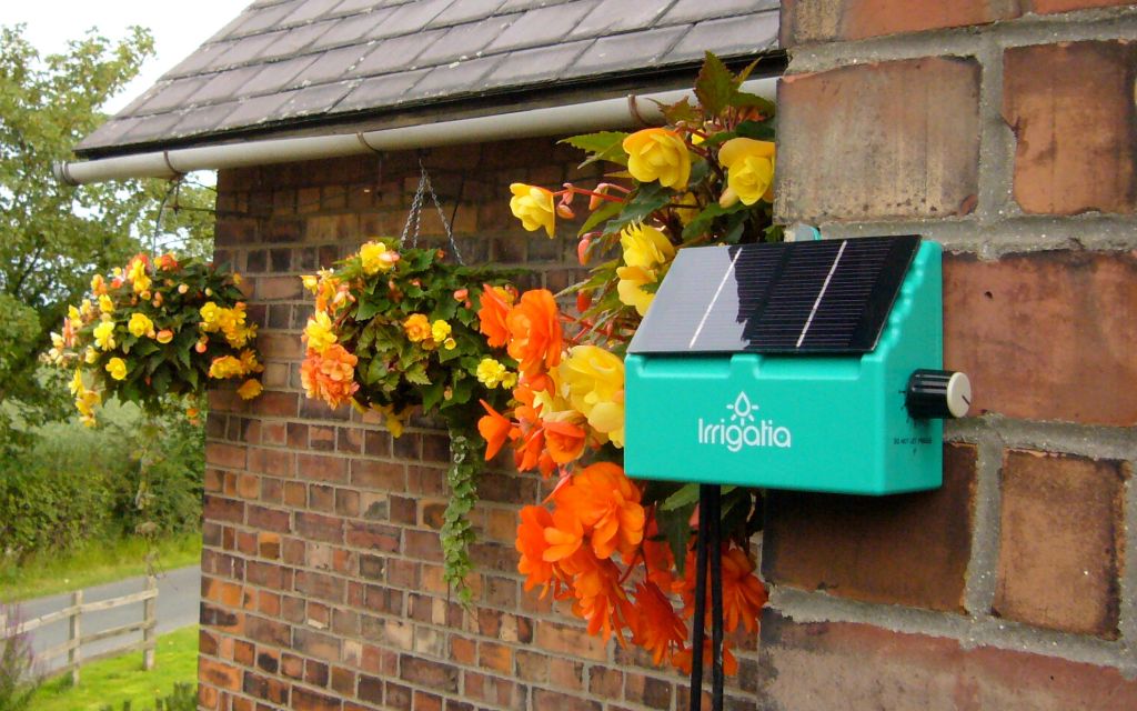 Hanging baskets line the eavestrough of a house with an Irrigatia solar panel in the foreground.