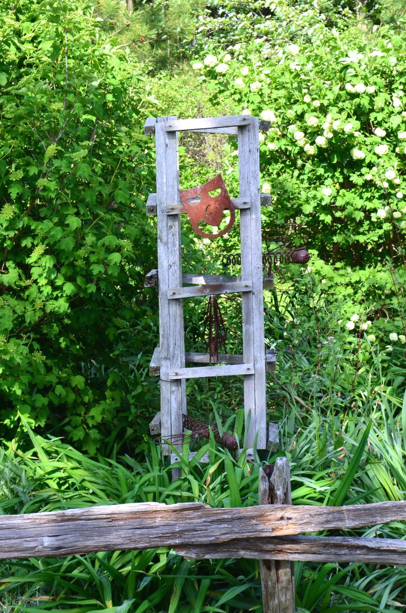 A wooden garden trellis is decorated with mask and pieces of metal.