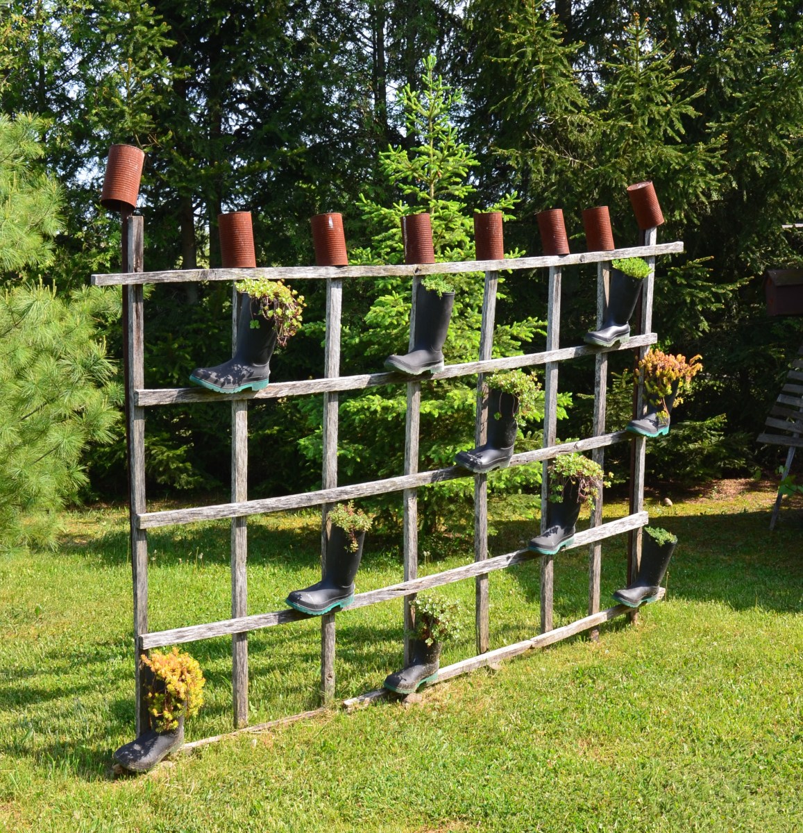 A handmade trellis is finished with pots and boots filled with plants.