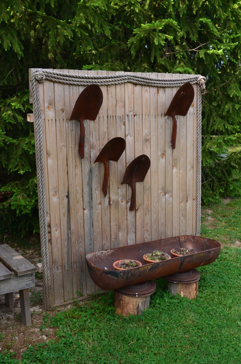 A wooden freestanding panel in a garden showcases old shovels.