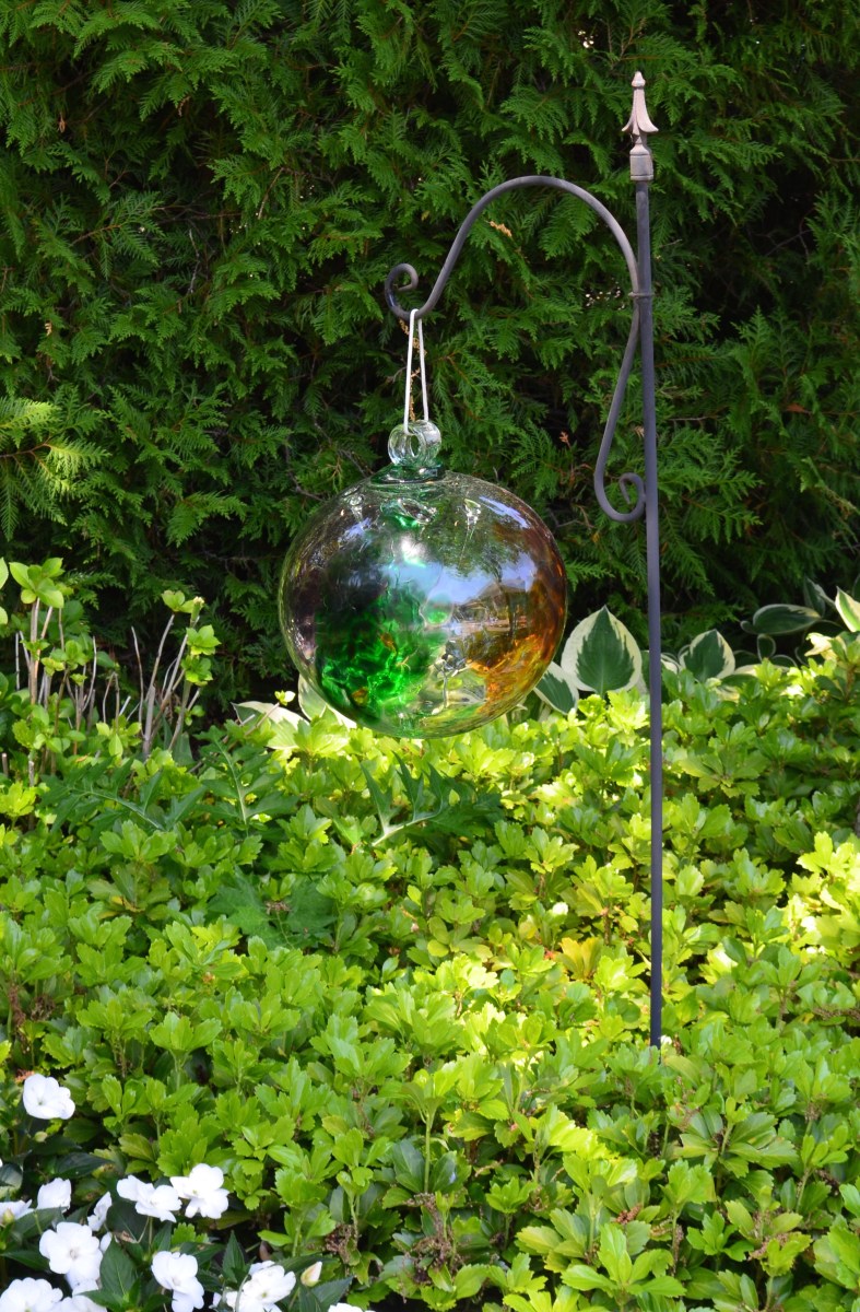 A reflective glass ball hangs in a garden bed.
