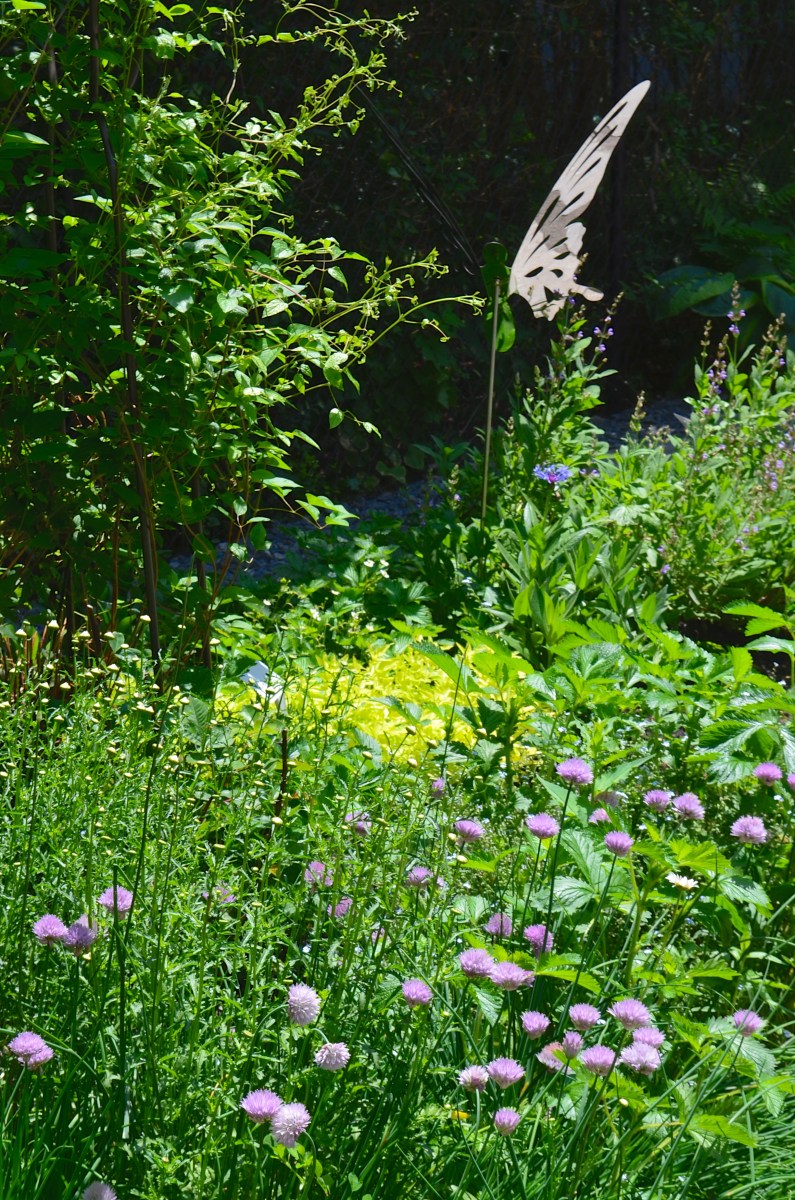 A garden bed with perennials and shrubs has sculptures of shining butterflies
