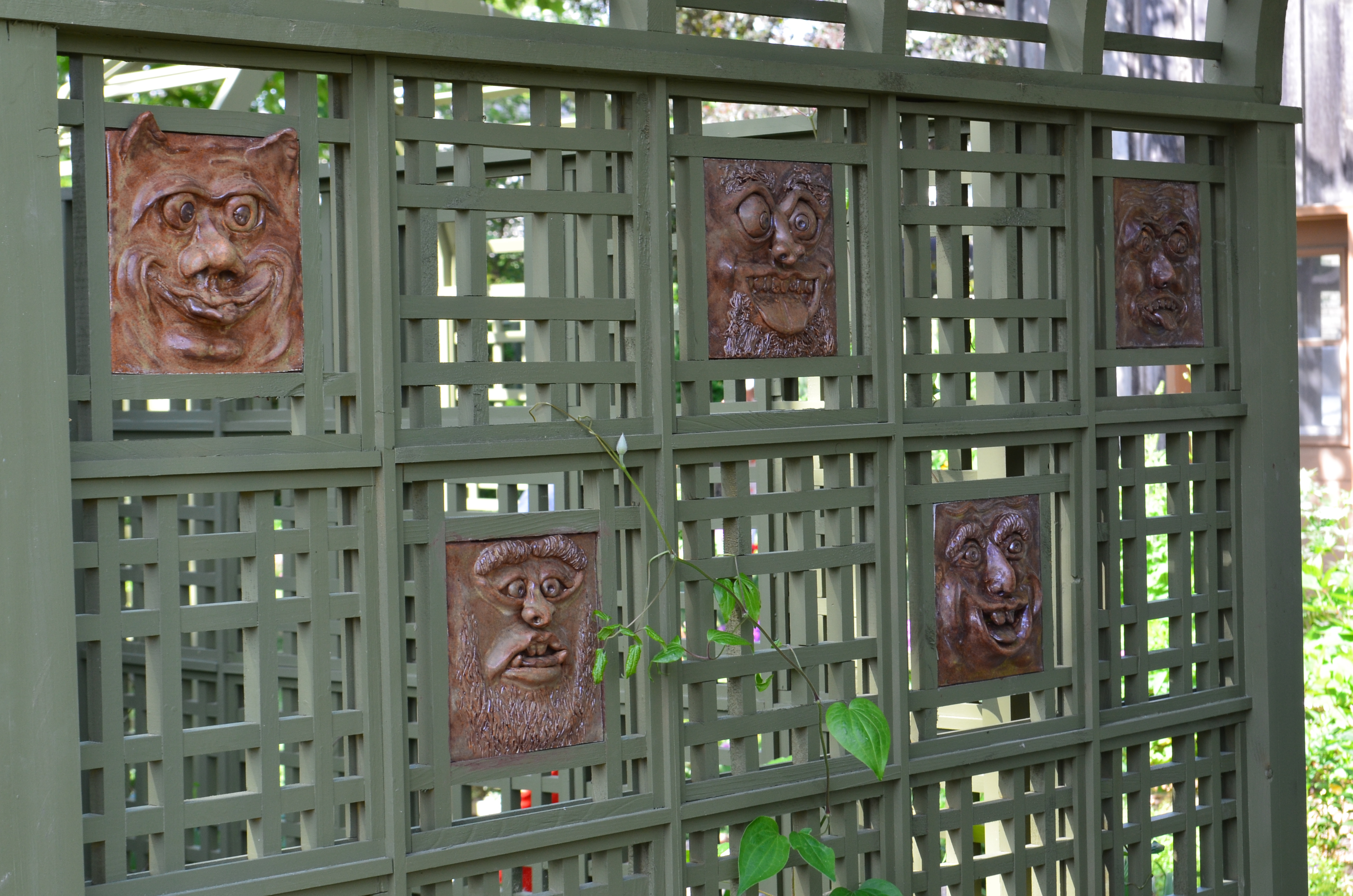 A collection of ceramic faces line the interior of a latticed archway in a garden.