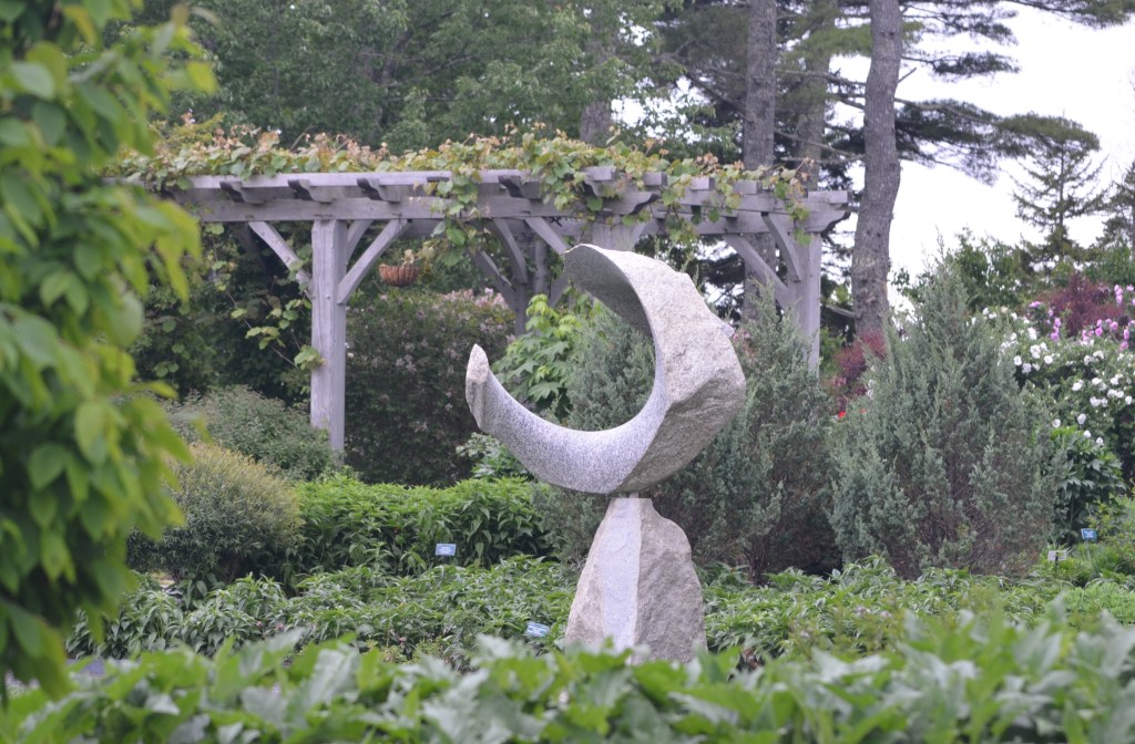 A stone sculpture in a garden with a gazebo in the background