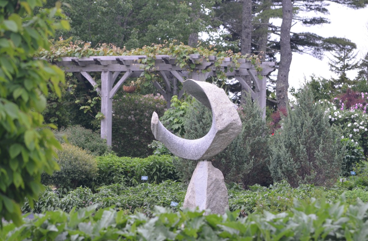 A stone sculpture in a garden with a gazebo in the background