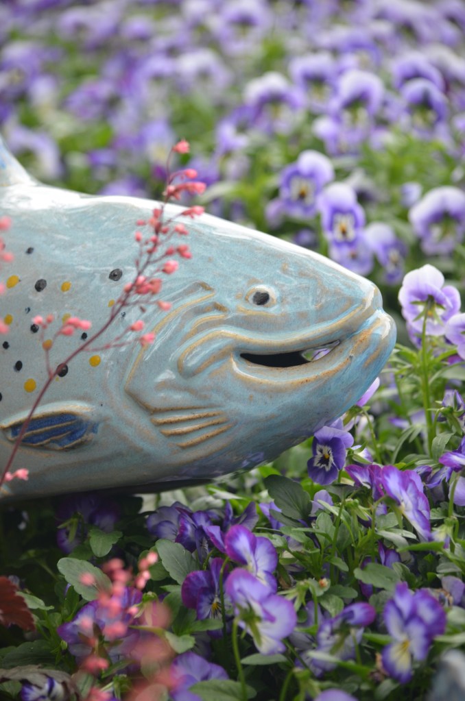 A blue ceramic fish in a bed of purple flowers