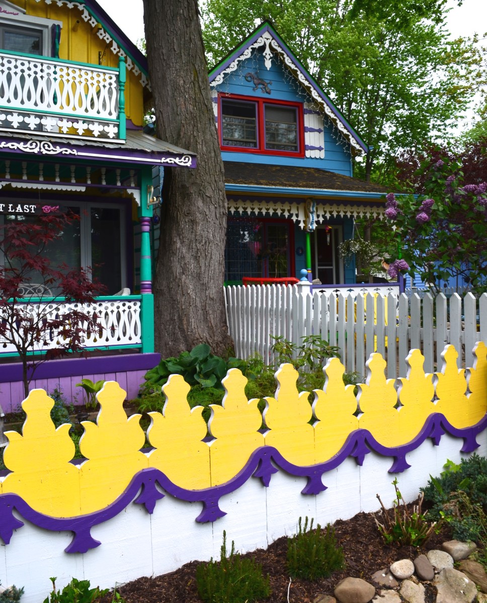 A fence is intricately carved and painted yellow, white and purple.