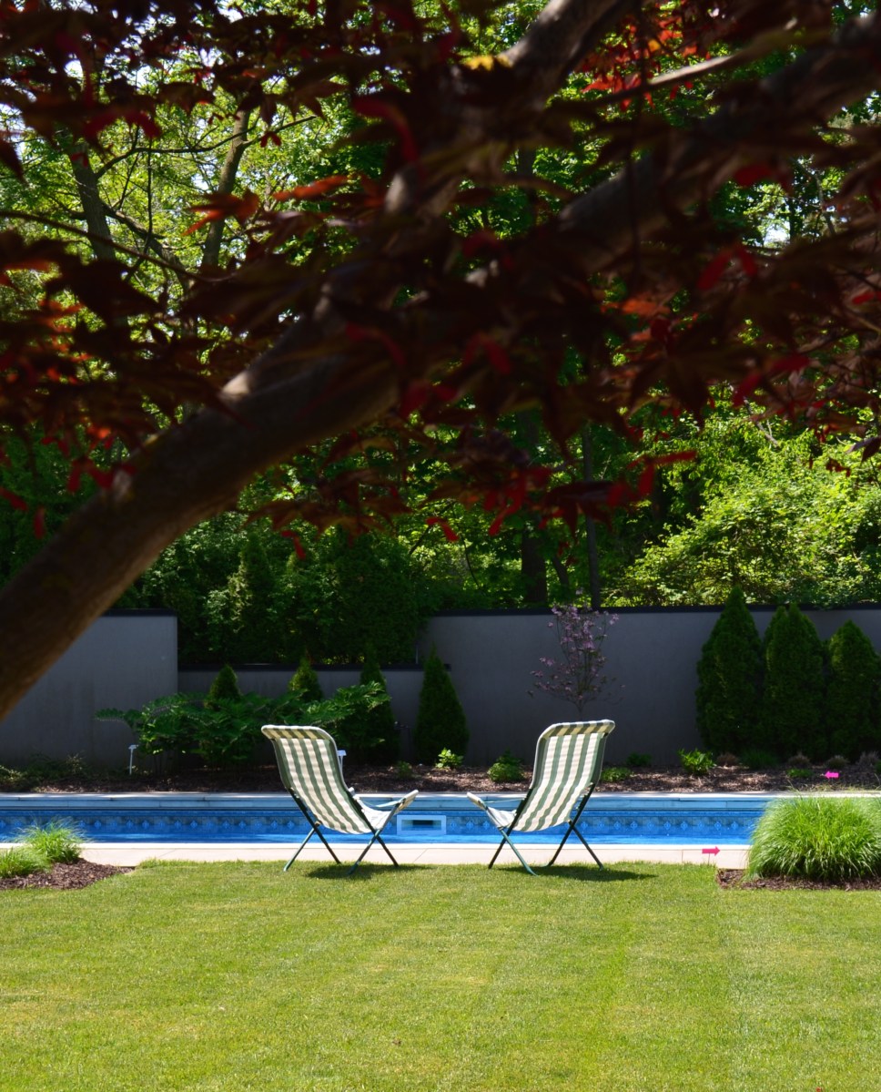 Two lawn chairs are set by a large pool enclosed by high walls.