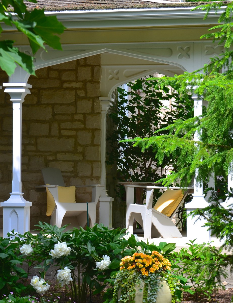 Two wooden chairs on a porch have pillows matching the flowers in the garden alongside.
