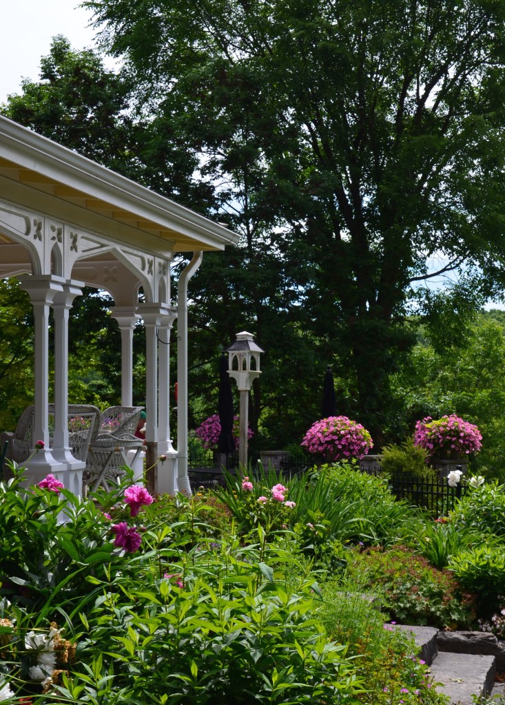 A house with porch overlooks a terraced area with bright flowers in containers