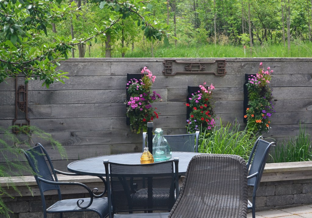 An outdoor wall separates a quiet seating area from the driveway of a modern rustic home and garden