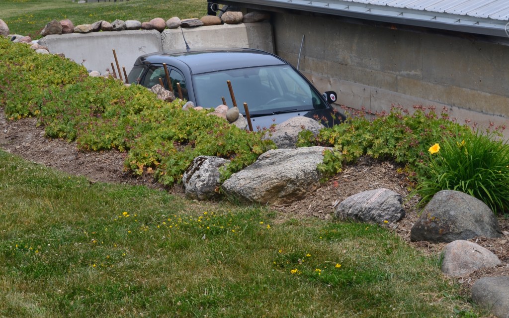 A car in a driveway is barely seen beyond a retaining wall with decorative rock garden