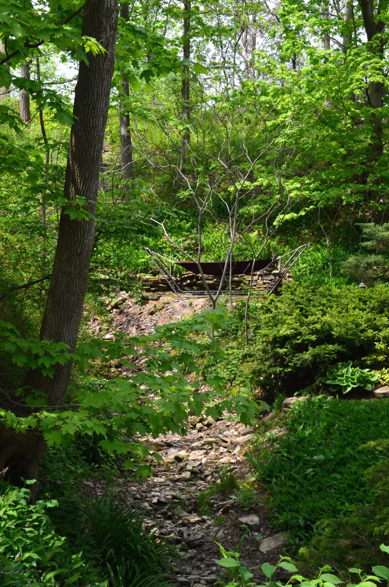 A hammock in a steel frame is situated on a wooded hill overlooking a dry creek.
