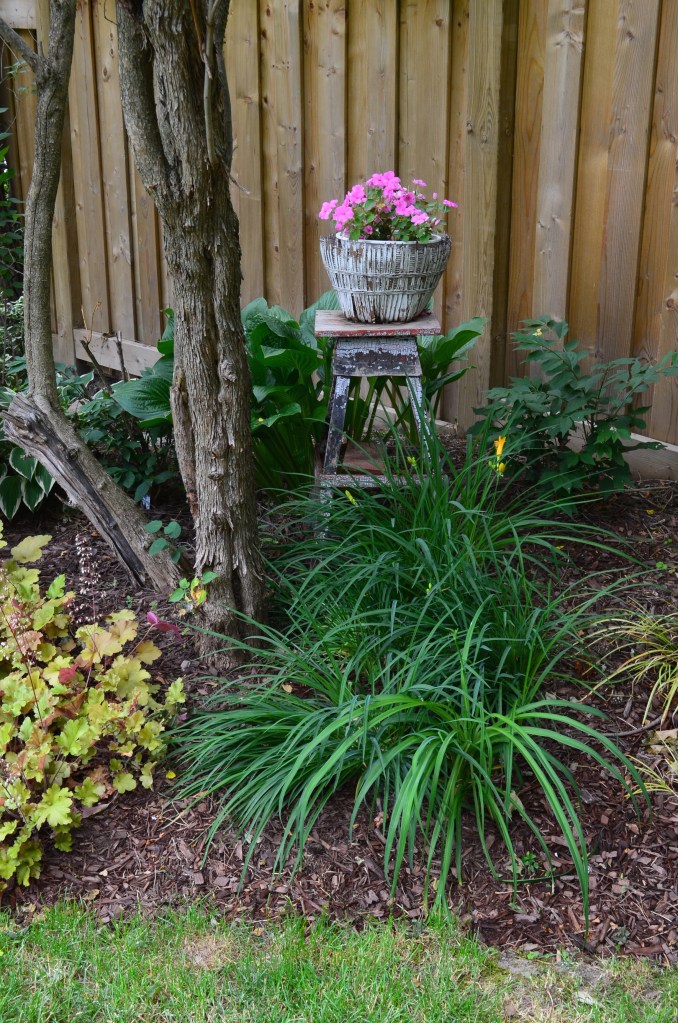 A small container on a wooden stool in the flower bed of a woodland garden