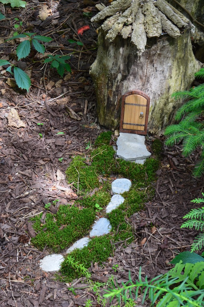 A tree stump fairy house in a woodland style garden.