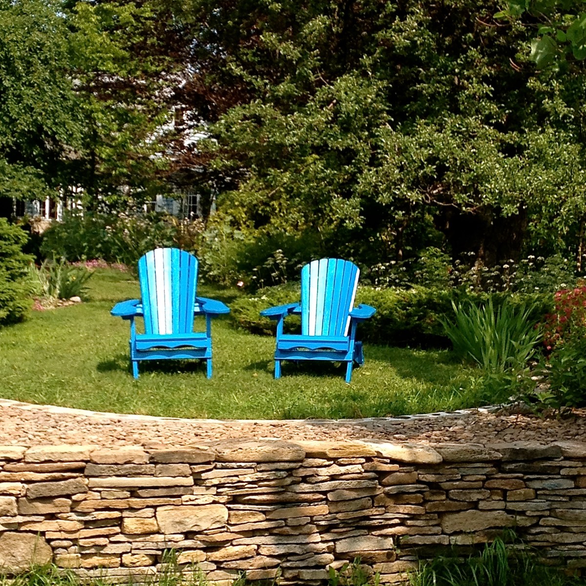 Two garden chairs are placed on a terraced lawn lined with a stone abutment.