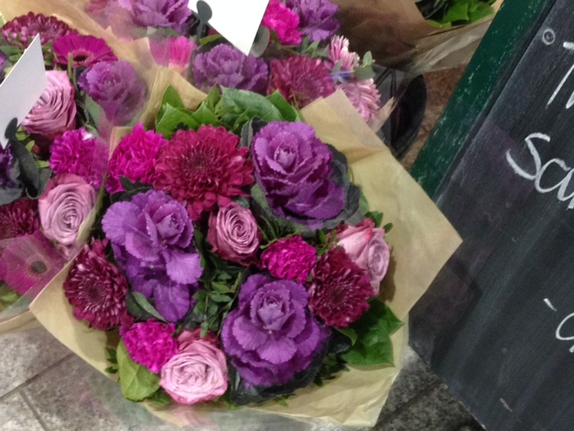 A bouquet of roses, mums and small ornamental cabbage heads with a fall decor theme.