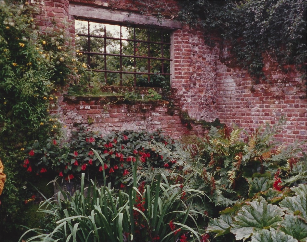A window in an old brick wall which separates two gardens at Sissinghurst.