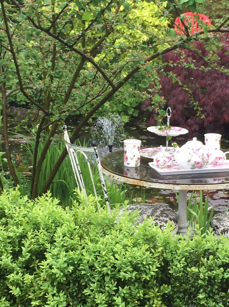 A back garden filled with plants features an all-weather tea table.