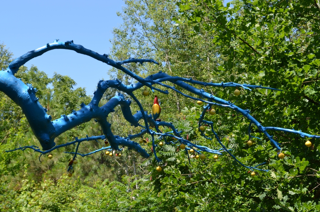 A dead tree branch painted blue is decorated with a painted bird.